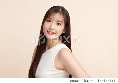 A beautiful young Asian woman with clean, fresh skin against a beige background. Skincare, facial treatment, cosmetology, beauty, and spa. An elegant portrait of an Asian woman. 127187141