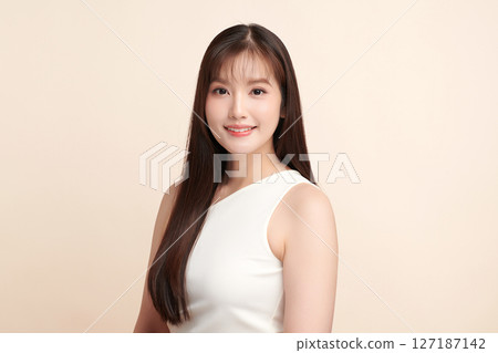 A beautiful young Asian woman with clean, fresh skin against a beige background. Skincare, facial treatment, cosmetology, beauty, and spa. An elegant portrait of an Asian woman. 127187142