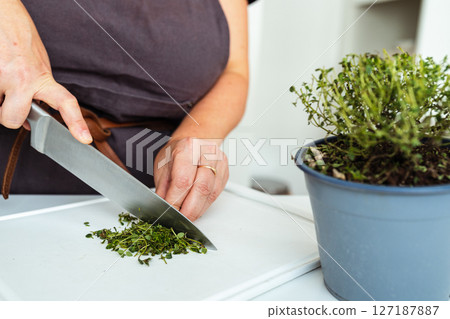 woman in brown apron cuts herbs on cutting board with sharp kitchen knife woman in brown apron cuts herbs on cutting board with sharp kitchen knife 127187887