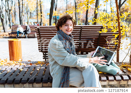 Happy teenage girl in autumn park on video call through laptop 127187914