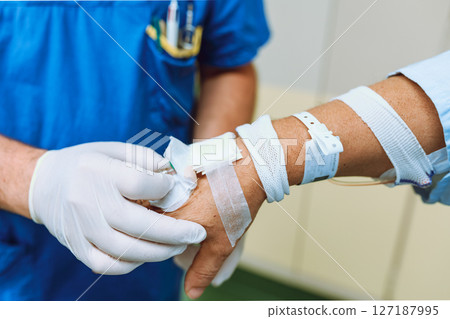 Doctor's hands in medical gloves checking venous catheter on patient's arm 127187995