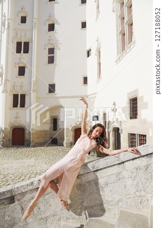 Ballerina balancing gracefully on stone edge near ornate castle wall 127188052