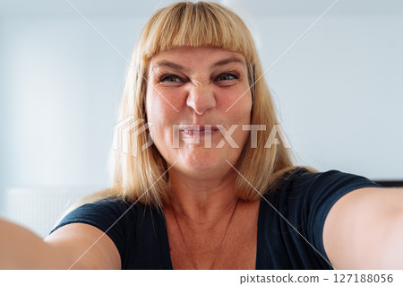 Portrait middle-aged woman, blonde, grimacing in front mirror Portrait middle-aged woman, blonde, grimacing in front mirror 127188056