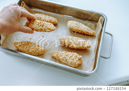 Raw frozen breaded chicken pieces on a baking sheet. 127188154