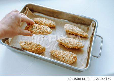 Raw frozen breaded chicken pieces on a baking sheet. 127188169