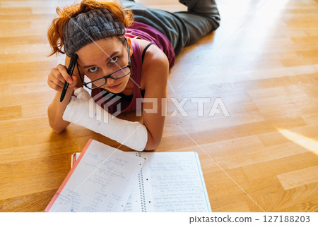 Teenage girl with broken arm in cast, wearing glasses, doing homework, at home Teenage girl with broken arm in cast, wearing glasses, doing homework, at home 127188203