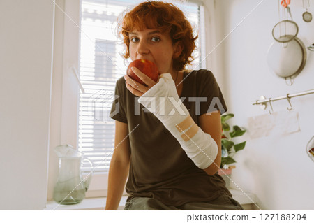 teenage girl with broken arm in cast in kitchen sitting on countertop eating apple teenage girl with broken arm in cast in kitchen sitting on countertop eating apple 127188204