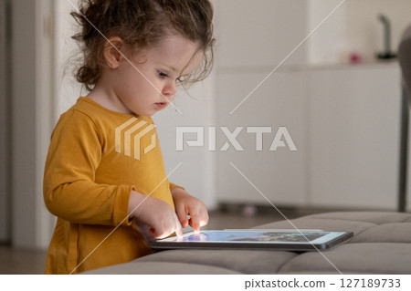 Child exploring creativity with a drawing app on a tablet in a modern living room environment. Child exploring creativity with a drawing app on a tablet in a modern living room environment. 127189733