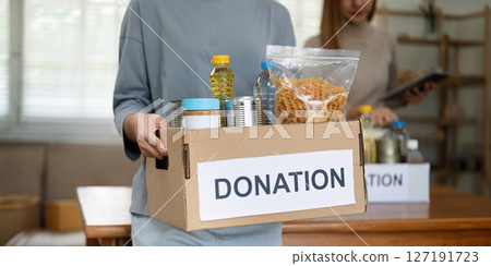 charity, donation and volunteering concept. Volunteer prepare foodstuff box containing food to donate to people poor, disaster victim at home 127191723