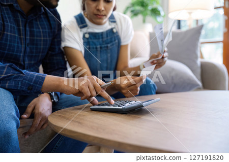 Indian married couple calculating bills, discussing planning budget together, serious wife and husband looking at calculator, checking finances Indian married couple calculating bills, discussing planning budget together, serious wife and husband looking at calculator, checking finances 127191820
