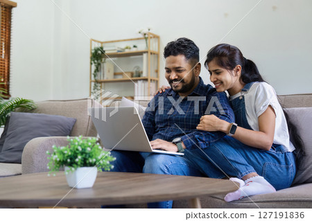 Happy indian Couple Using Laptop Browsing Internet Together on sofa at home Happy indian Couple Using Laptop Browsing Internet Together on sofa at home 127191836