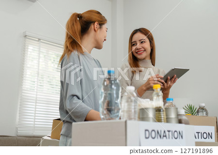charity, donation and volunteering concept. Volunteer prepare foodstuff box containing food to donate to people poor, disaster victim at home charity, donation and volunteering concept. Volunteer prepare foodstuff box containing food to donate to people poor, disaster victim at home 127191896