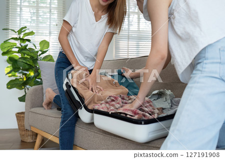 Preparation for vacation. Happy friends woman packing and trying to close suitcase on sofa Preparation for vacation. Happy friends woman packing and trying to close suitcase on sofa 127191908