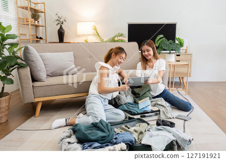Friend using tablet for booking vacation at travel agency or making hotel reservation online and packing clothes into suitcase at home, planning travel holiday Friend using tablet for booking vacation at travel agency or making hotel reservation online and packing clothes into suitcase at home, planning travel holiday 127191921