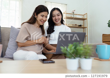Mother and adult daughter sitting on the sofa together, mother and daughter using laptop to surf website together Mother and adult daughter sitting on the sofa together, mother and daughter using laptop to surf website together 127191979