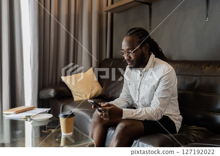 Young African American man relaxing on soft at home, texting messaging on smartphone. man using mobile phone chatting online message, shopping online from home Young African American man relaxing on soft at home, texting messaging on smartphone. man using mobile phone chatting online message, shopping online from home 127192022