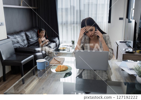 Business woman working at home. working woman talk on mobile and working on laptop and take care of her daughter during summer Business woman working at home. working woman talk on mobile and working on laptop and take care of her daughter during summer 127192222
