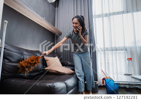 Young woman chit chat with friend on mobile while cleaning house on weekend Young woman chit chat with friend on mobile while cleaning house on weekend 127192281