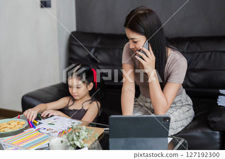 Businessman working at home. working woman talk on mobile and working on tablet and take care of her daughter during summer Businessman working at home. working woman talk on mobile and working on tablet and take care of her daughter during summer 127192300