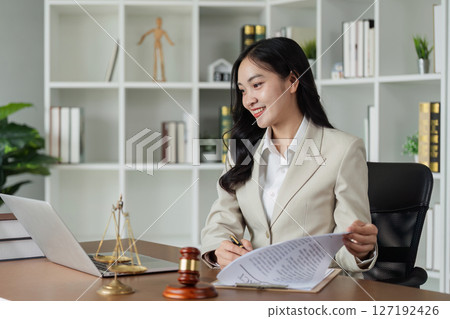 Lawyer sitting at desk and reviewing client document and working on laptop Lawyer sitting at desk and reviewing client document and working on laptop 127192426