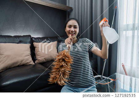 Asian woman happily use feather pick as microphone while cleaning house on the weekend Asian woman happily use feather pick as microphone while cleaning house on the weekend 127192535