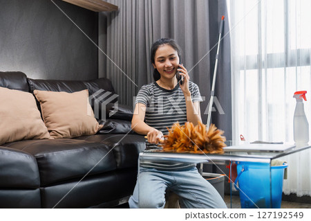 Young woman chit chat with friend on mobile while cleaning house on weekend Young woman chit chat with friend on mobile while cleaning house on weekend 127192549
