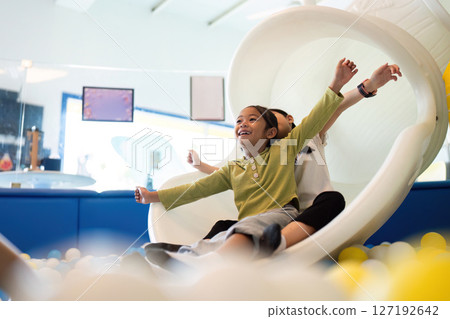 Sliding Fun. Two girls enjoying a playful slide in a colorful indoor playground. 127192642