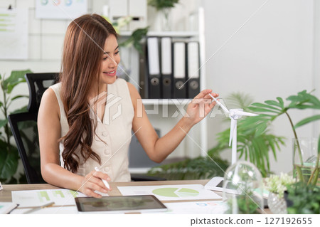 Sustainable Business Engagement. A woman smiling while interacting with a wind turbine model. Sustainable Business Engagement. A woman smiling while interacting with a wind turbine model. 127192655