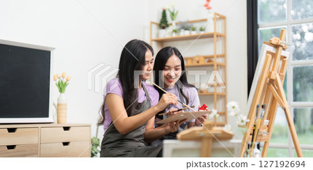 Couple Sharing Artistic Moments. Two young women collaborating on a painting project in a bright room. Couple Sharing Artistic Moments. Two young women collaborating on a painting project in a bright room. 127192694