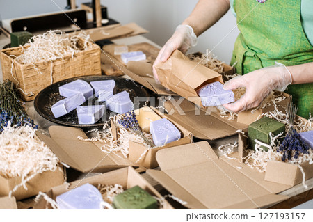 Person packs lavender soap into a kraft paper bag surrounded by shredded filler and handmade bars. Handmade product shipping, indie beauty dispatch, craft brand logistics, eco-packaging workflow Person packs lavender soap into a kraft paper bag surrounded by shredded filler and handmade bars. Handmade product shipping, indie beauty dispatch, craft brand logistics, eco-packaging workflow 127193157