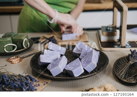 Person in green apron stamps a lavender soap bar by hand on a wooden board. Handmade soap branding, artisan process, small batch skincare, craft identity Person in green apron stamps a lavender soap bar by hand on a wooden board. Handmade soap branding, artisan process, small batch skincare, craft identity 127193164