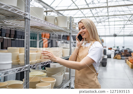 A woman is on the phone at a shop, looking at a variety of flowerpots. A woman is on the phone at a shop, looking at a variety of flowerpots. 127193515
