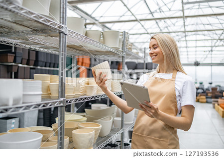 A shop worker is reviewing flower pots with a tablet. The store has a variety of different flower pots. The shop has a glass ceiling. A shop worker is reviewing flower pots with a tablet. The store has a variety of different flower pots. The shop has a glass ceiling. 127193536