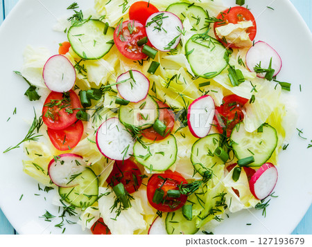 Plate with fresh spring salad of sliced radish, cherry tomatoes, cucumber, greens and iceberg salad covered in olive oil, top view of plate with vitamin meal. Plate with fresh spring salad of sliced radish, cherry tomatoes, cucumber, greens and iceberg salad covered in olive oil, top view of plate with vitamin meal. 127193679