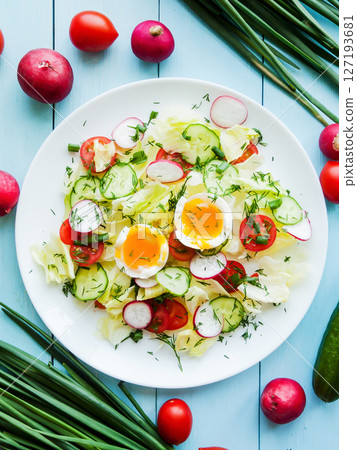 Plate with fresh spring salad of radish, cherry tomatoes, cucumber, greens iceberg and boiled eggs salad in olive oil, top view of plate with vitamin meal. 127193681