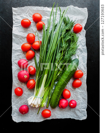 Fresh red cherry tomatoes, green leek, radish and cucumber on the parchment on table background, top view of vegetables covered with water drops. Fresh red cherry tomatoes, green leek, radish and cucumber on the parchment on table background, top view of vegetables covered with water drops. 127193683