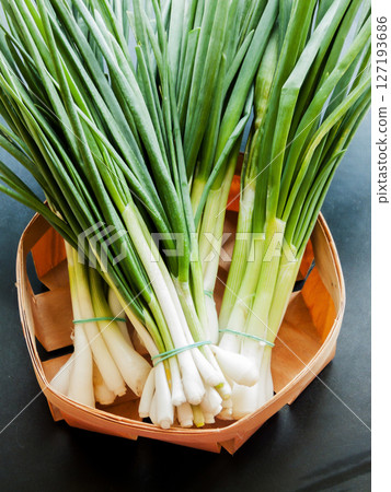 Fresh green leek onion in the basket on the white wooden background, top view bunch of greens on the table. 127193686