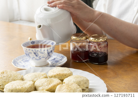 Freshly baked tea scones with jam on them, lifted by hand Tea scones with teapot and teacup Freshly baked tea scones with jam on them, lifted by hand Tea scones with teapot and teacup 127193711