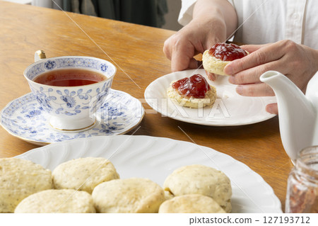 Freshly baked tea scones with jam on them, lifted by hand Tea scones with teapot and teacup Freshly baked tea scones with jam on them, lifted by hand Tea scones with teapot and teacup 127193712