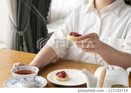 Freshly baked tea scones with jam on them, lifted by hand Tea scones with teapot and teacup 127193714