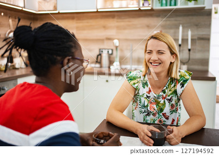 Two friends share laughter and coffee in a cozy modern kitchen 127194592