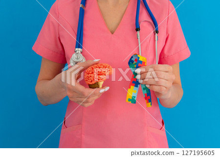 Female doctor is holding anatomical model human brain with Puzzle pattern ribbon . Help and care concept Female doctor is holding anatomical model human brain with Puzzle pattern ribbon . Help and care concept 127195605
