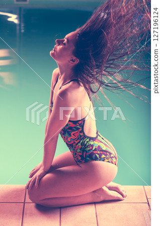 Woman in swimsuit sit at edge swimming pool side view. 127196124