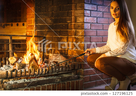 Woman with fire iron poker at home fireplace. 127196125