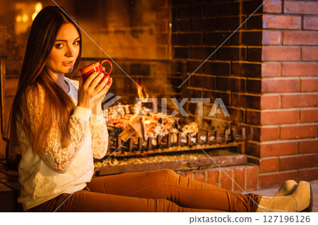 Woman drinking hot coffee relaxing at fireplace. Woman drinking hot coffee relaxing at fireplace. 127196126