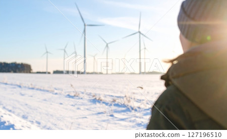 Woman near a wind turbine in a snowy winter landscape, symbolizing renewable energy and green technology 127196510