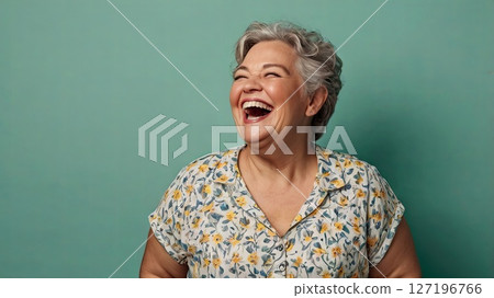 Beautiful middle aged woman in light clothes on isolated mint background smiling and laughing loudly. Concept of happy retirement, harmony, self-acceptance by an older woman. 127196766