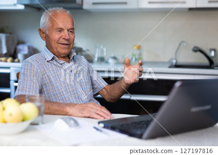 Retiree doing online shopping using laptop while sitting in the kitchen of home 127197816