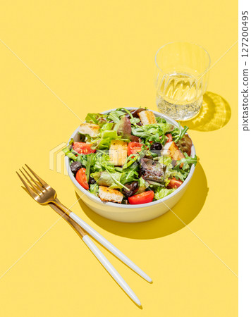 Vegetable salad with lettuce, tomatoes, croutons and olives in a bowl on a yellow background 127200495