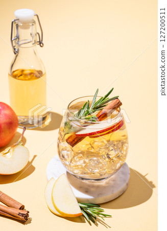 Apple cocktail or cider in a glass with ice, cinnamon and rosemary on a marble stand 127200511